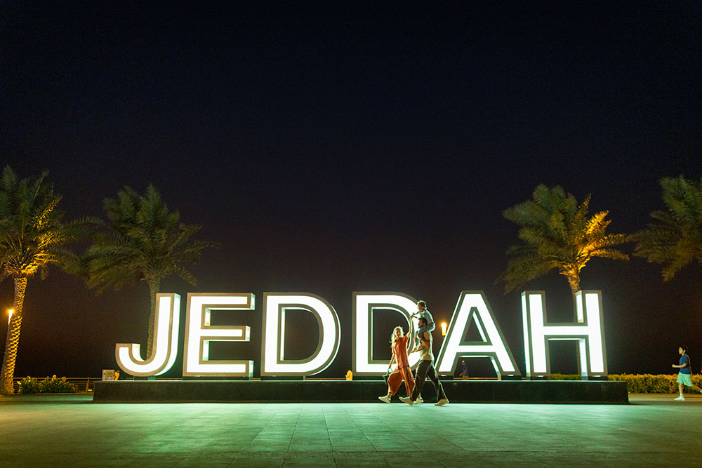 Eine Familie spaziert am Strand vor dem „Jeddah“-Schriftzug entlang.